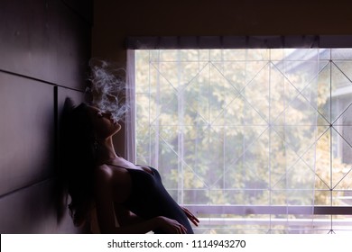 Portrait charming beautiful model woman. Attractive beautiful sexy women is smoking cigarette or weed in dark room at house. Gorgeous woman feels like a dreaming, mind drifting or floating in the air