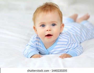 Portrait of a charming blue-eyed 7 month old baby lying in bed in a striped body