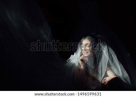 Portrait of charming bride enveloped in a veil. Beuatiful bride hidden under the veil. Beautiful bride in veil. Close up. Beauty woman. Wedding morning closeup on black background.
