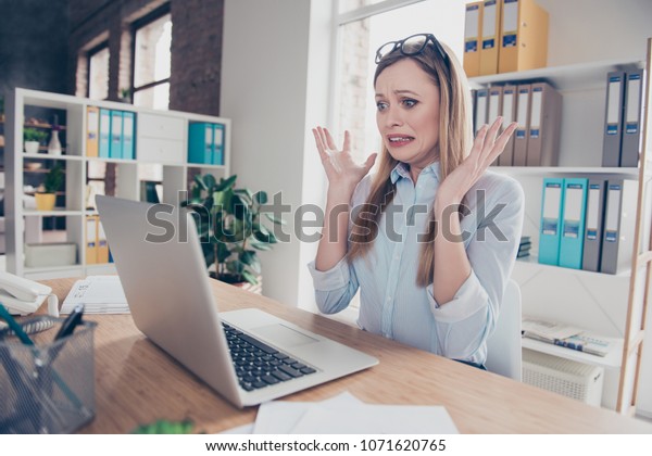 魅力的で 感情的 心配性 神経質な女性のポートレートで 頭に眼鏡をかけ 手で髪型のジェスチャー コンピューターを見て 何かが故障し 時間に間に合わず 机に座っている の写真素材 今すぐ編集