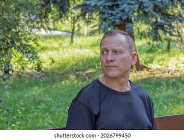 Portrait Of A Charming, Handsome, Serious, Mature Man In A Black T-shirt, Looking To The Side, Against The Background Of A Green Park