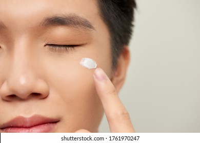 Portrait of a charming handsome young guy has healthy perfect skin, cream on his face, holds moisturizing cream on his face.