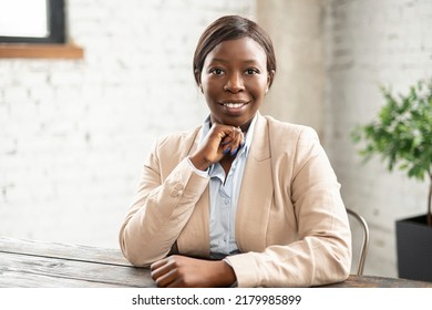 Portrait Of Charming Positive African-American Businesswoman Wearing Stylish Smart Casual Attire Sitting At The Desk. Confident Lady Female Office Employee Looks At The Camera.