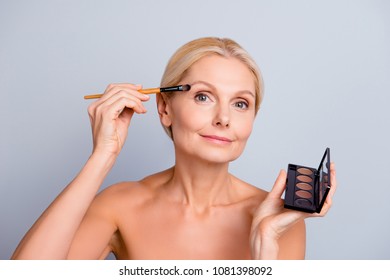 Portrait Of Charming Pretty Trendy Senior Woman Applying Eye Shadow With Brush Having Dark Palette In Hand Looking At Camera Isolated On Grey Background, Making Festive Visage