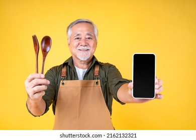 Portrait charming retired asian elder man has a white mustache and beard wearing apron holding fork spoon and smartphone order food in mobile online application isolated yellow background - Powered by Shutterstock