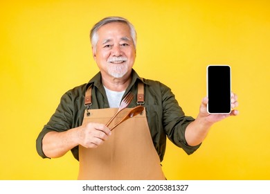 Portrait charming retired asian elder man has a white mustache and beard wearing apron holding fork spoon and smartphone order food in mobile online application isolated yellow background - Shutterstock ID 2205381327