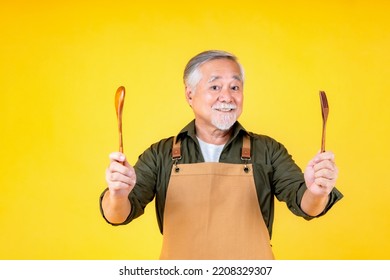 Portrait charming retired asian elder man has a white mustache and beard wearing apron holding fork spoon yellow background. - Shutterstock ID 2208329307