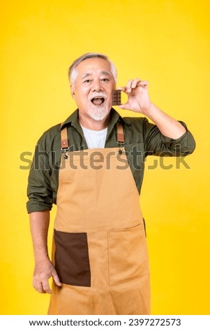 Portrait charming retired asian elder man has a white mustache and beard wearing apron hold chocolate yellow background.