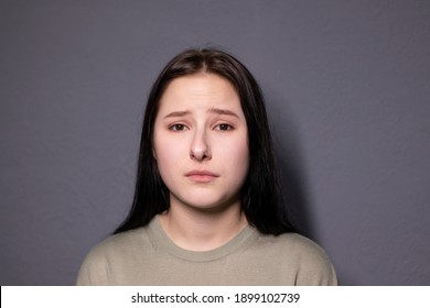 Portrait Of Charming Sad Brunette Woman In Marsh Color T-shirt On Grey Wall Background. Actress Acting, Emotion. Copy Space