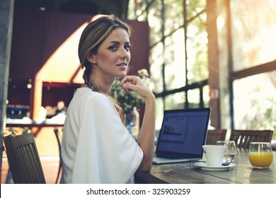 Portrait of charming smiling businesswomen posing while resting after work on her portable laptop computer during coffee break, young pretty female using net-book while sitting in modern cafe interior - Powered by Shutterstock