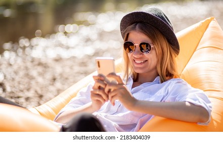 Portrait of charming smiling woman in sunglasses using cellphone and write messages to friends while lying on inflatable mattress on summer beach - Powered by Shutterstock