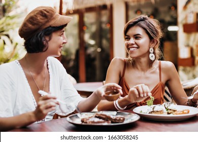 Portrait Of Charming Tanned Women In Good Mood Eating Tasty Food In Street Cafe. Attractive Brunette Girls Gossip And Smile Outside