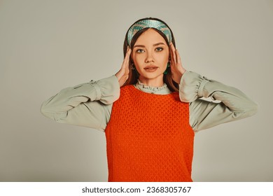 portrait of charming woman in orange dress adjusting colorful headband on grey, old-fashioned style