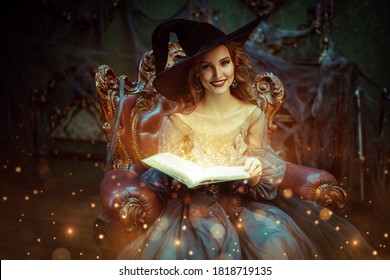 Portrait of a charming woman witch in a hat and beautiful dress sitting in an armchair with a book of spell in the old castle. Halloween. Celebration.