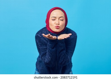 Portrait of charming young Asian woman holding palms sending air kisses in front of camera