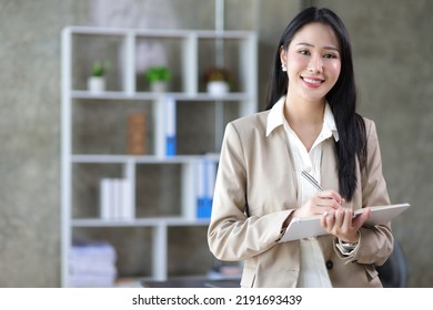 Portrait Of A Charming Young Woman Businessman In The Office Standing Holding A Notepad With A Pen Looking At The Camera.