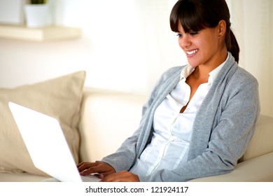 Portrait Of A Charming Young Woman Sitting On Couch Reading The Laptop Screen At Home Indoor