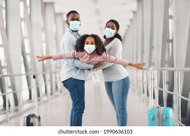 Portrait Of Cheerful African American Family In Medical Masks Having Fun, Parents Holding Daughter, Girl Spreading Hands As Wings Imitating Plane, Pretending Flying. Three People Going On Journey