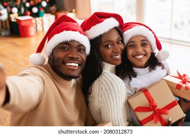 Portrait of cheerful African American family in red Santa Claus hats celebrating Christmas, taking selfie, smiling excited teenager daughter holding present box, looking at camera posing for photo - Powered by Shutterstock