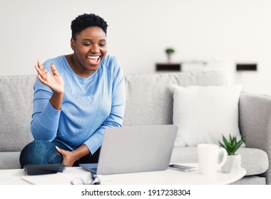 Portrait Of Cheerful African American Woman Having Online Conference With Friends, Using Laptop, Gesturing And Waving At Laptop Screen. Happy Black Female Making Videocall, Talking And Sitting On Sofa