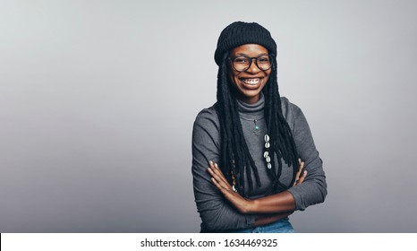 Portrait of cheerful african female having long dreadlocks looking at camera. Smiling african woman with her arms crossed isolated on grey background. - Powered by Shutterstock