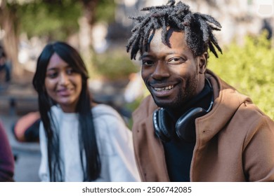 Portrait of a cheerful African man with dreadlocks wearing headphones, accompanied by a smiling woman with long dark hair. Diverse couple enjoying urban outdoor setting - friendship and inclusivity. - Powered by Shutterstock