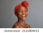 Portrait of cheerful african mature woman with headscarf against grey wall. Middle aged black woman laughing, copy space. Happy smiling black lady wearing traditional african scarf and looking at came