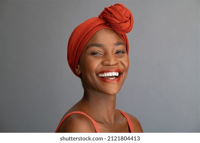 Portrait of cheerful african mature woman with headscarf against grey wall. Middle aged black woman laughing, copy space. Happy smiling black lady wearing traditional african scarf and looking at came