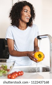 Portrait Of A Cheerful Afro American Woman Washing Vegetables To Make A Salad At The Kitchen