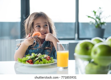 Portrait of cheerful asian girl eating salad with joy. She is looking aside with curiosity and smiling