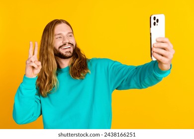 Portrait of cheerful attractive guy hold smart phone make selfie demonstrate v-sign isolated on yellow color background