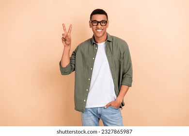 Portrait of cheerful attractive man toothy smile hand fingers demonstrate v-sign isolated on beige color background