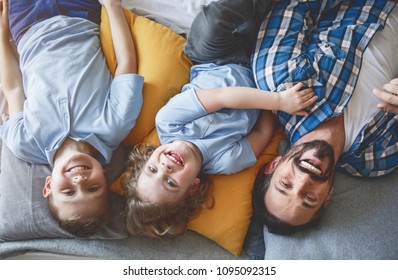 Portrait of cheerful bearded father relaxing on pillows with two little smiling kids. They looking at camera. Positive leisure at home concept - Shutterstock ID 1095092315