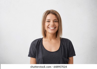 Portrait of cheerful beautiful woman with trendy hairdo having dark charming eyes and engaging smile posing in studio over white background. People, happiness, emotions and lifestyle concept