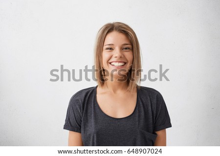 Portrait of cheerful beautiful woman with trendy hairdo having dark charming eyes and engaging smile posing in studio over white background. People, happiness, emotions and lifestyle concept