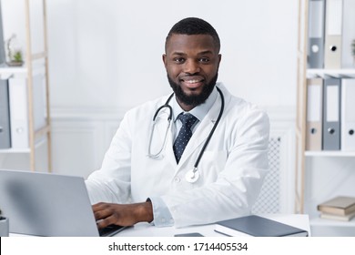 Portrait of cheerful black doctor sitting at his workplace - Powered by Shutterstock