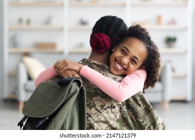 Portrait Of Cheerful Black Girl With Bushy Hair Teenager Hugging Her Mother Soldier And Smiling, Looking At Copy Space. Child Enjoying Reunion With Mom Returned From Military Service, Home Interior