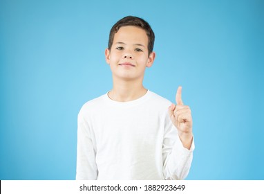 Portrait Of Cheerful Boy With Good Idea - Isolated Over Blue Background. 10 Year Old Kid Pointing Finger Up. Child Points By Finger Upward. Cheerful Boy Shows Something