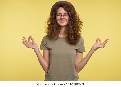 A Portrait Of Cheerful Brunette Woman With Curly Hair, She Makes Okay Gesture, Smiles And Thinking Of Something Good, Isolated Over Yellow Background, Body Language Concept