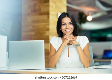 Porträt einer fröhlichen Geschäftsfrau, die am Tisch im Büro sitzt und die Kamera ansieht
