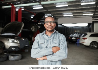 Portrait of cheerful car mechanic in grey overall standing in garage - Powered by Shutterstock