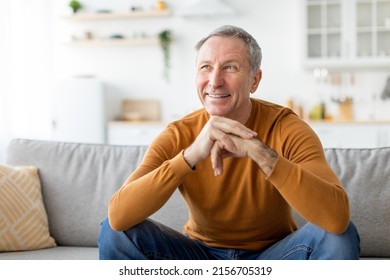 Portrait of cheerful casual senior man smiling and looking away, sitting on sofa couch in living room. Excited mature adult male resting at home dreaming about something pleasant, free copy space - Powered by Shutterstock