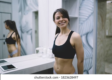 Portrait Of Cheerful Caucasian Female Looking At Camera Satisfied With Training Results And Slimming In Gym Happy Beautiful Woman In Sporttop Preparing For Workout In Modern Locker Room With Mirror