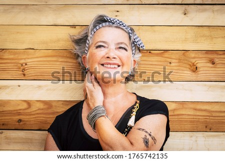Portrait of cheerful caucasian senior happy woman with wood background - alternative and young old female smile and enjoy - tatooed skin for diversity concept and age - youthful lifestyle