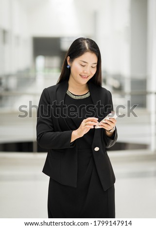 Portrait of a cheerful and confident businesswoman in business suit dialing cellphone to text messege in the business building. Business stock photo.