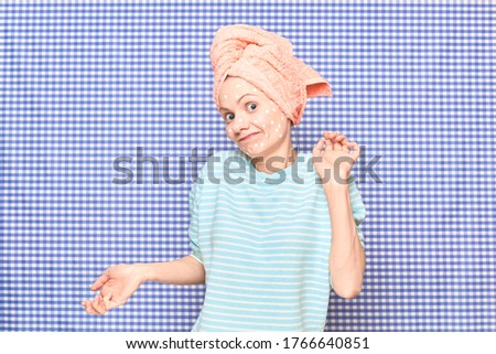 Portrait of cheerful confused puzzled girl with anti-acne skincare product on face, with towel on head, standing over shower curtain background. Care for acne-prone skin. Beauty concept
