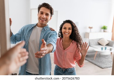 Portrait of cheerful couple inviting guests to enter home, happy young guy and lady standing in doorway of modern flat, looking out, man shaking hands, meeting new neighbors or friends - Shutterstock ID 2075626783