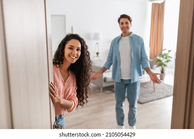 Portrait Of Cheerful Couple Inviting Guests To Enter Home, Happy People Standing In Doorway Of Modern Flat, Looking Out Waiting For Visitor To Come In, Receiving Friend, Lady Peeking Out Of Front Door