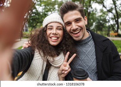 Portrait of cheerful couple man and woman 20s taking selfie photo while sitting on bench in green park - Powered by Shutterstock