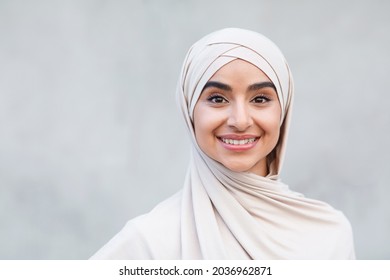 Portrait of cheerful cute attractive young arabian islamic female in hijab looks at camera. Headshot of modern blogger, student or business woman isolated on gray background, close up, empty space